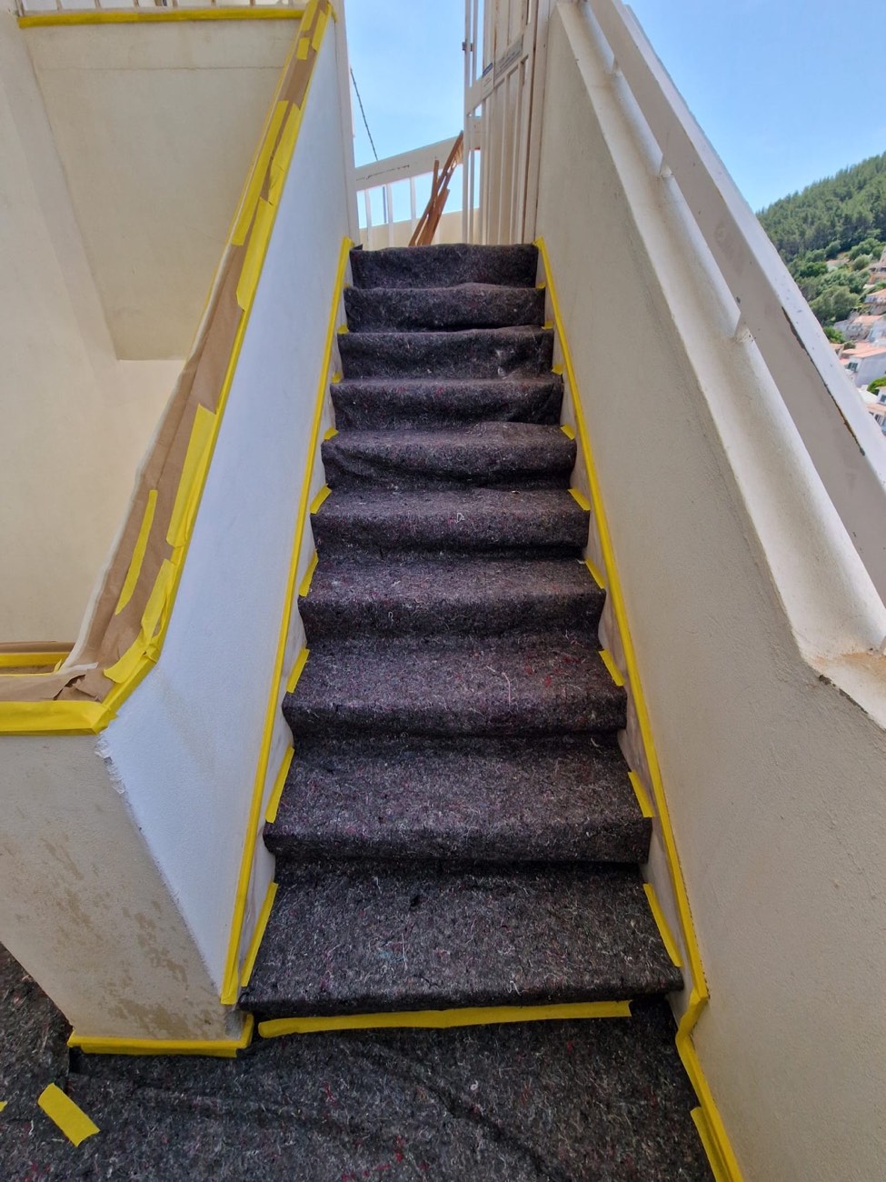 Escada exterior com degraus protegidos e fita nas paredes antes da pintura