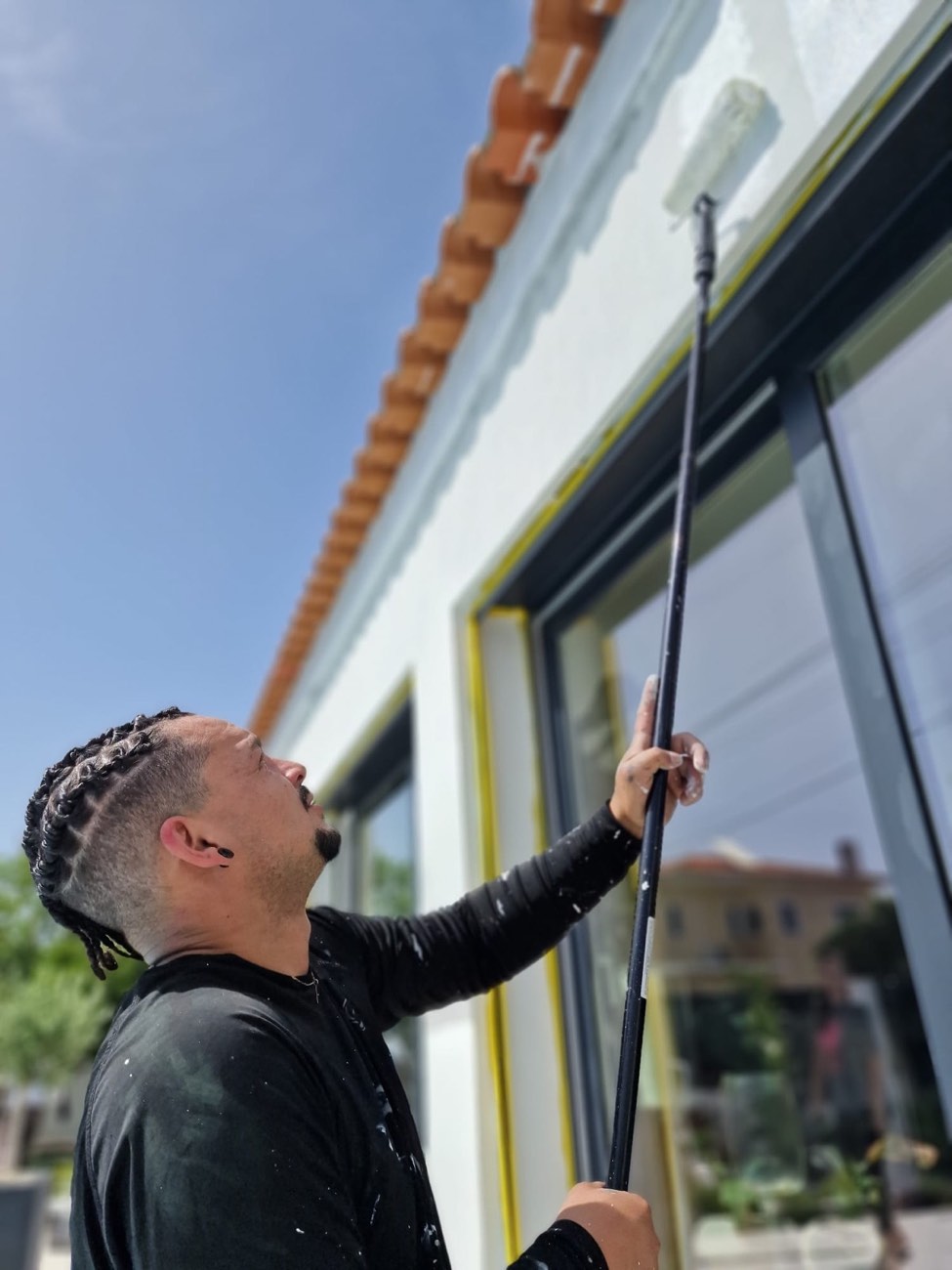 Pintor a pintar a fachada junto às janelas, com os caixilhos protegidos com fita